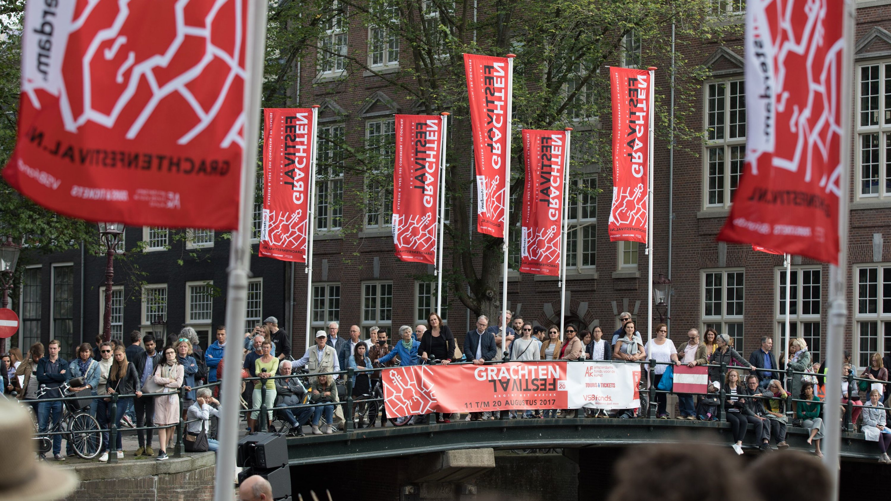 Veel mensen staan op een brug te luisteren naar een klassiek concert op het water